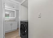 Thumbnail 14 of 111 - A washing machine is placed in a room with a white wall and a door leading to another room.