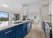 Thumbnail 1 of 111 - A kitchen with blue cabinets and a window overlooking a green landscape.