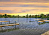 Thumbnail 65 of 111 - A serene lake with wooden benches and a building in the distance under a twilight sky.