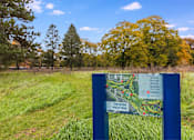 Thumbnail 66 of 111 - A sign for the River Walk Trail stands in a grassy field.