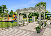 Thumbnail 77 of 111 - A white pergola is over a patio with a table and chairs.