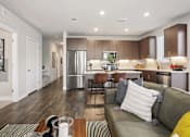 Thumbnail 21 of 26 - A modern kitchen and living room with a grey couch and wooden floors.