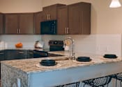 Thumbnail 8 of 17 - A kitchen with a granite countertop and black chairs.