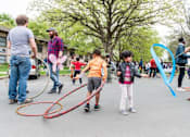 Thumbnail 23 of 24 - A group of people are playing with hula hoops in a street.