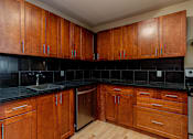 Thumbnail 6 of 23 - A kitchen with wooden cabinets and black countertops.