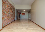 Thumbnail 12 of 23 - A long hallway with a brick wall on the left and wooden floors.