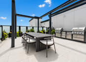Thumbnail 7 of 40 - A table and chairs are on a patio with a grill and a building in the background.