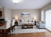 Thumbnail 19 of 20 - A living room with a grey couch, a coffee table, and a painting on the wall.