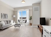 Thumbnail 4 of 24 - A living room with a grey couch, a black TV, and a large window with a view of the city.