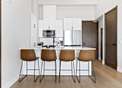 Thumbnail 7 of 24 - A kitchen with white cabinets and a bar area with brown chairs at The Woods at 180 Kanata Avenue, Kanata, Ontario