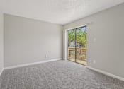 Thumbnail 25 of 39 - A room with a carpeted floor and a sliding glass door leading to a balcony.