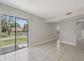 Thumbnail 32 of 39 - A spacious room with tiled flooring and a view of a street through a sliding glass door.