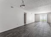 Thumbnail 7 of 18 - A large empty room with a wooden floor and a hanging light fixture.