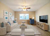 Thumbnail 1 of 13 - A living room with a white couch, a coffee table, and a flat screen TV.