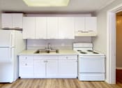 Thumbnail 4 of 9 - A white kitchen with a refrigerator, stove, and sink.