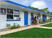 Thumbnail 10 of 12 - A white building with blue doors and windows has a sign on the left side.