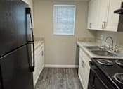 Thumbnail 6 of 39 - A black refrigerator stands in a kitchen with white cabinets and a black stove.