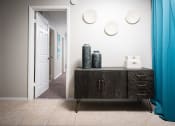 Thumbnail 9 of 33 - a hallway with a dresser and a door to a room with blue curtains at Fairways of Inverrary, Lauderhill, FL, 33319