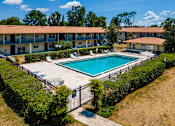 Thumbnail 20 of 21 - A swimming pool surrounded by a fence and bushes in front of a building.