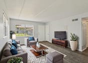 Thumbnail 1 of 15 - A living room with a grey couch, a coffee table, and a television.