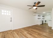Thumbnail 6 of 18 - an empty living room with a ceiling fan and a kitchen in the background
