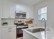 Thumbnail 9 of 18 - A kitchen with white cabinets and a stove top oven.