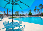 Thumbnail 33 of 95 - a swimming pool with tables and chairs under an umbrella at Presidio Palms Apartments, Arizona
