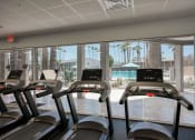 Thumbnail 59 of 95 - a gym with cardio machines and a view of a swimming pool at Presidio Palms Apartments, Tucson