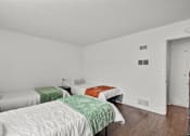 Thumbnail 16 of 28 - Three beds with green and orange bedspreads in a white room.
