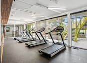 Thumbnail 17 of 31 - A gym with treadmills and a view of the outside.