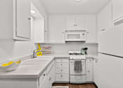 Thumbnail 11 of 28 - A white kitchen with a sink, stove, and cabinets.