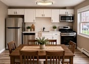 Thumbnail 2 of 14 - A kitchen with a table and chairs in the foreground and a refrigerator, microwave, oven, and sink in the background.
