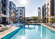 Thumbnail 32 of 61 - A swimming pool surrounded by lounge chairs and umbrellas in front of apartment buildings.