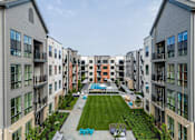 Thumbnail 58 of 61 - A view of a courtyard with a lawn and seating area surrounded by apartment buildings.