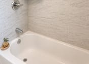 Thumbnail 7 of 14 - A white bathtub with a shower head and a shelf above it.