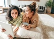 Thumbnail 78 of 80 - two women laying on the floor looking at a tablet computer