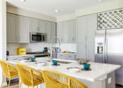 Thumbnail 32 of 44 - a kitchen with a large white island with yellow chairs and a stainless steel refrigerator