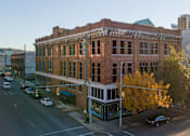 Thumbnail 4 of 26 - A large brick building with a green awning sits on a street corner.