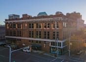 Thumbnail 6 of 26 - A large brick building with a green roof and a white car parked in front.