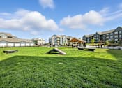 Thumbnail 52 of 59 - A park with a grassy area and benches in front of apartment buildings at The Garrison Luxury Apartment Homes, Fountain, CO 80817