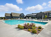 Thumbnail 47 of 59 - A large outdoor swimming pool surrounded by buildings and plants at The Garrison Luxury Apartment Homes, Fountain, CO 80817