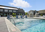 Thumbnail 41 of 59 - A pool with a wooden deck and a building in the background at The Garrison Luxury Apartment Homes, Fountain, CO 80817