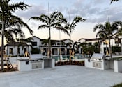 Thumbnail 3 of 17 - A white outdoor kitchen area with palm trees in the background.