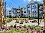Thumbnail 92 of 124 - Courtyard patio with swings fire table and palm trees at Velara Luxury Apartments, Ponte Vedra Beach, FL 32081