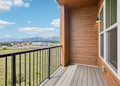 Thumbnail 24 of 24 - A balcony with a black railing and a wooden floor overlooks a grassy field and distant mountains.