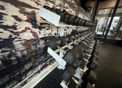 Thumbnail 20 of 56 - a row of dumbbells in a gym with a painting on the wall at Watermark at Steele Crossing, Fayetteville, AR