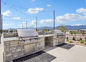 Thumbnail 16 of 24 - A stone BBQ grill with a metal lid is in the foreground with a fence and mountains in the background.