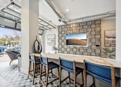 Thumbnail 27 of 59 - a long bar with blue chairs and a wall with a television at The Quarry Luxury Apartment Homes, Fort Collins, 80526