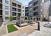 Thumbnail 3 of 32 - A modern outdoor seating area with a wooden swing set and a stone wall.at Refinery at Pointe17 Apartments, Phoenix, AZ, 85085