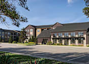 Thumbnail 1 of 24 - A large, modern building with a parking lot in front.